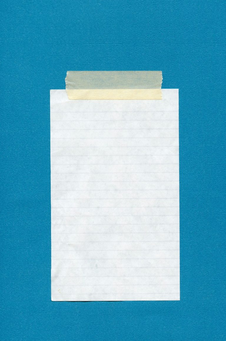 Blank lined paper attached with masking tape to a teal background.