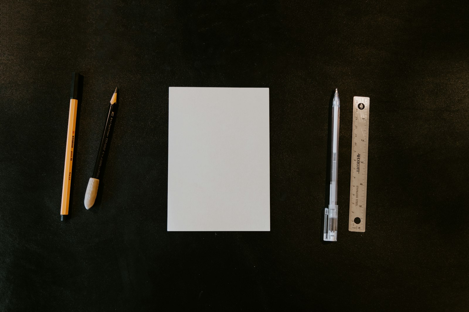 Blank paper with pens, a pencil and a ruler on a dark desk.