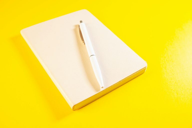 White pen on a closed cream notebook against a yellow background.