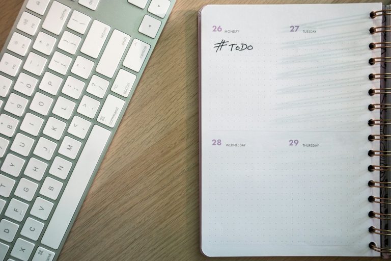 Open weekly planner marked To Do beside a white keyboard on a wooden desk.