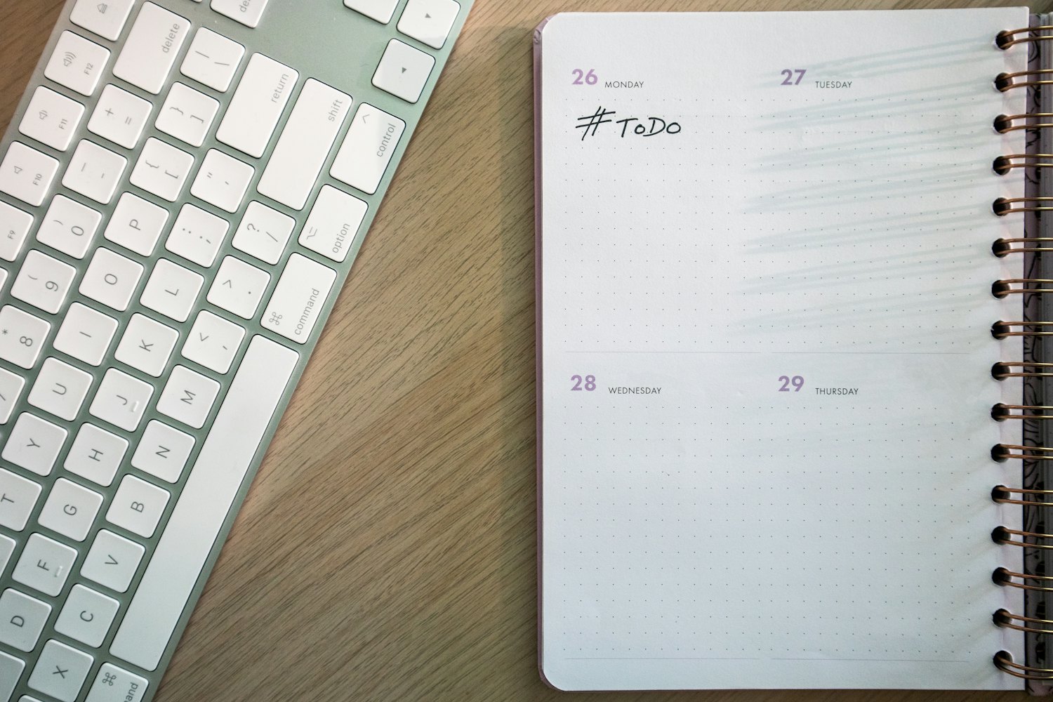 Open weekly planner marked To Do beside a white keyboard on a wooden desk.